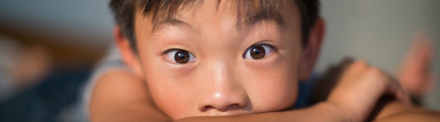 A close up of a child covering his mouth with his hand.