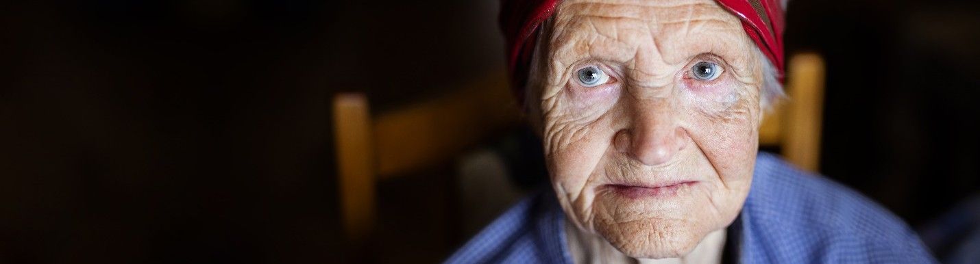 An elderly woman is sitting in a chair and looking at the camera.