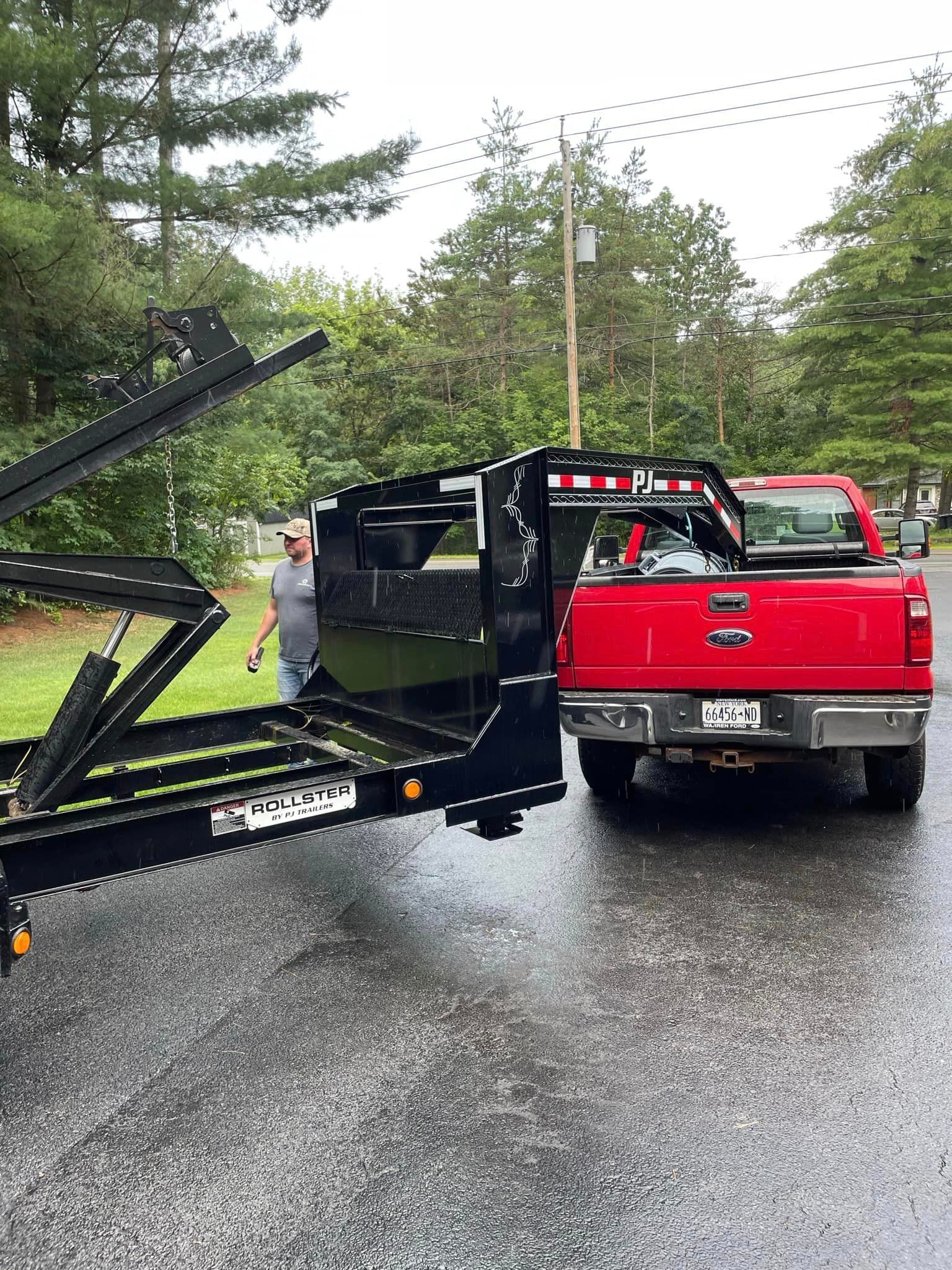 A man is standing next to a red truck with a trailer attached to it.