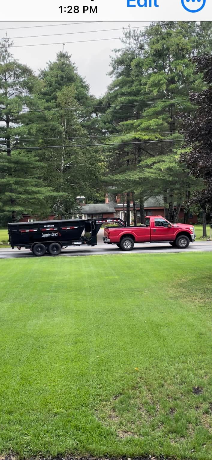 A red truck is pulling a black dumpster down a road.