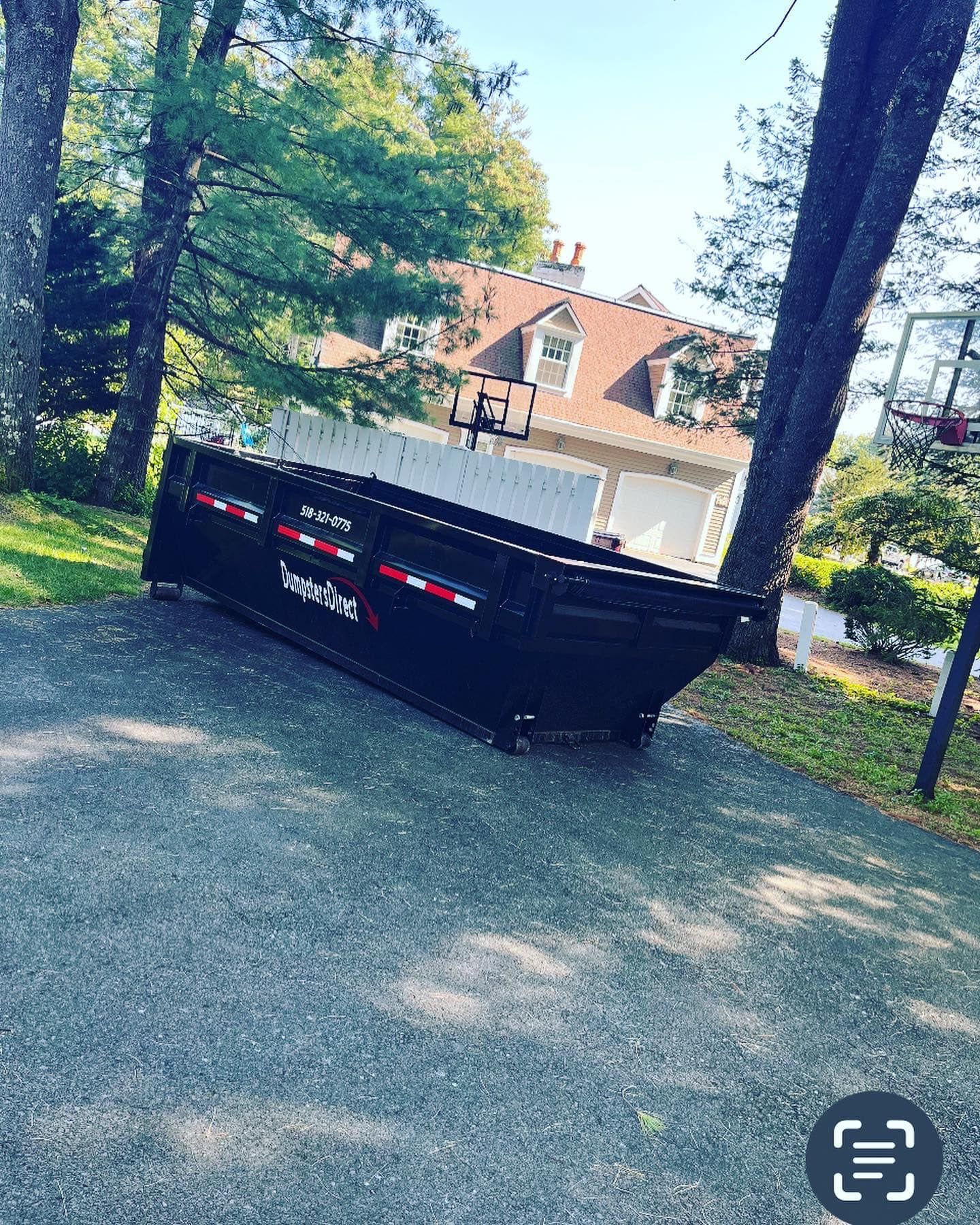 A dumpster is sitting on the side of a road in front of a house.