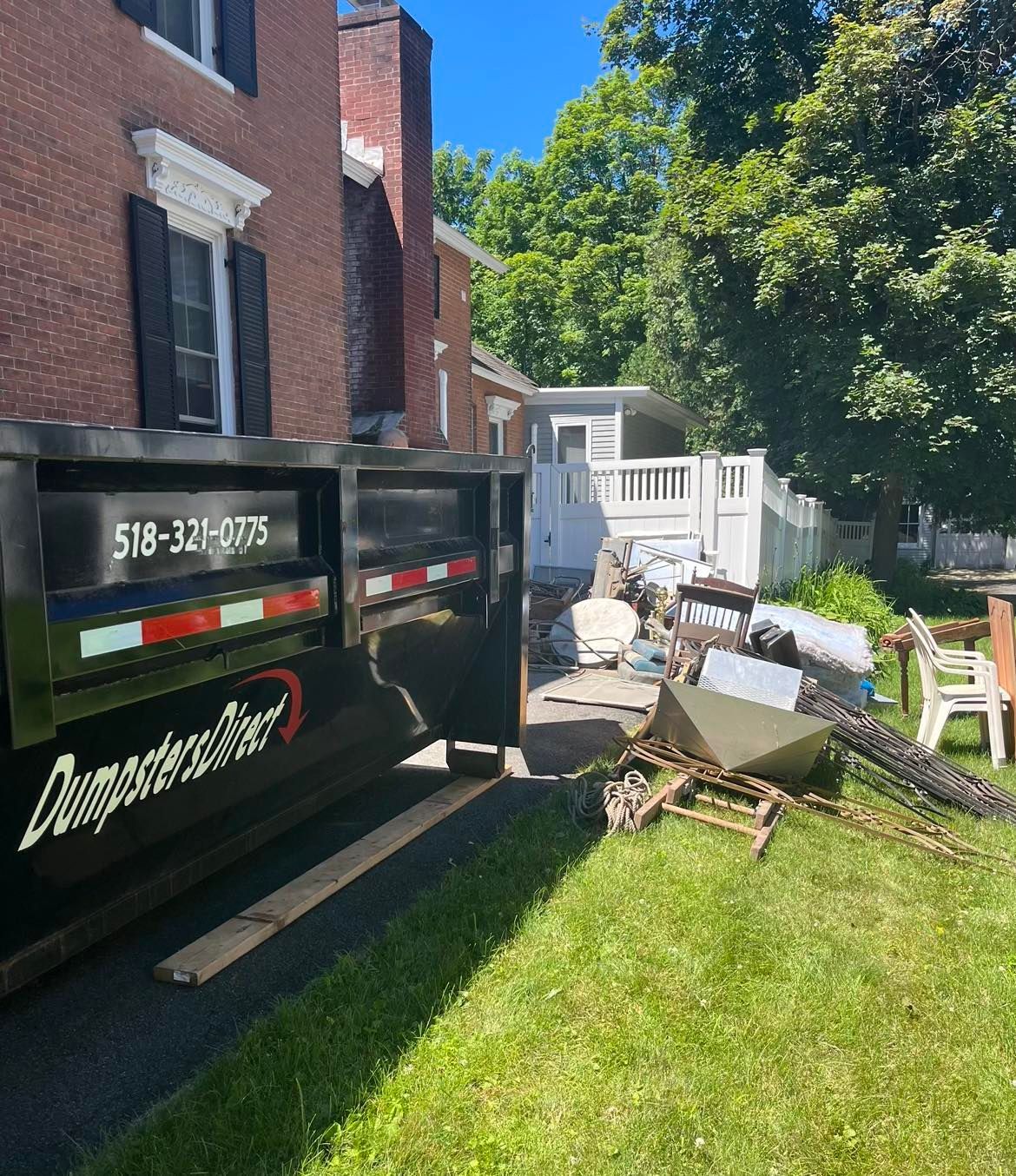 A dumpster is parked in front of a brick house.