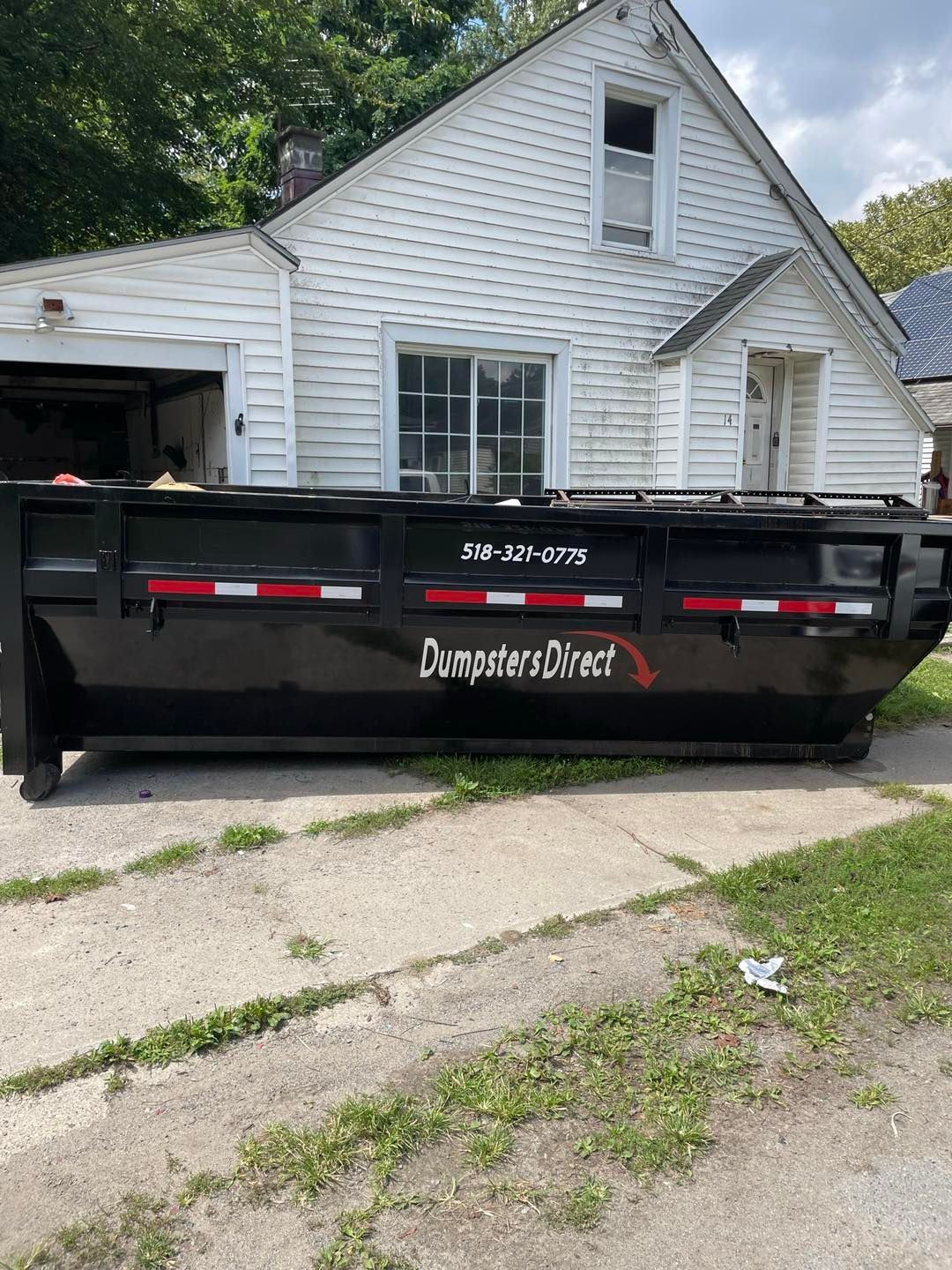 A dumpster is parked in front of a white house.