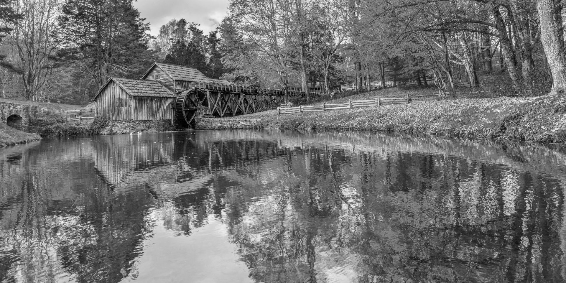 A black and white photo of a river with trees and a house in the background.