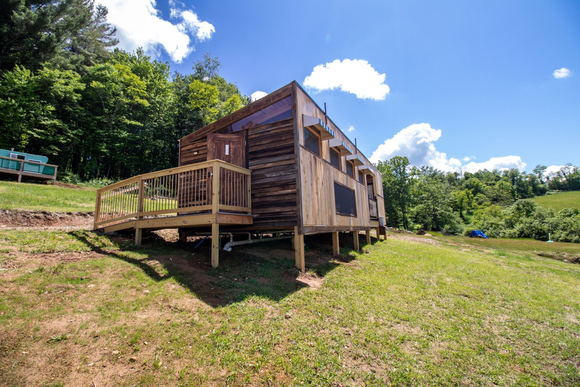 A small wooden house with a wooden deck is sitting on top of a grassy hill.