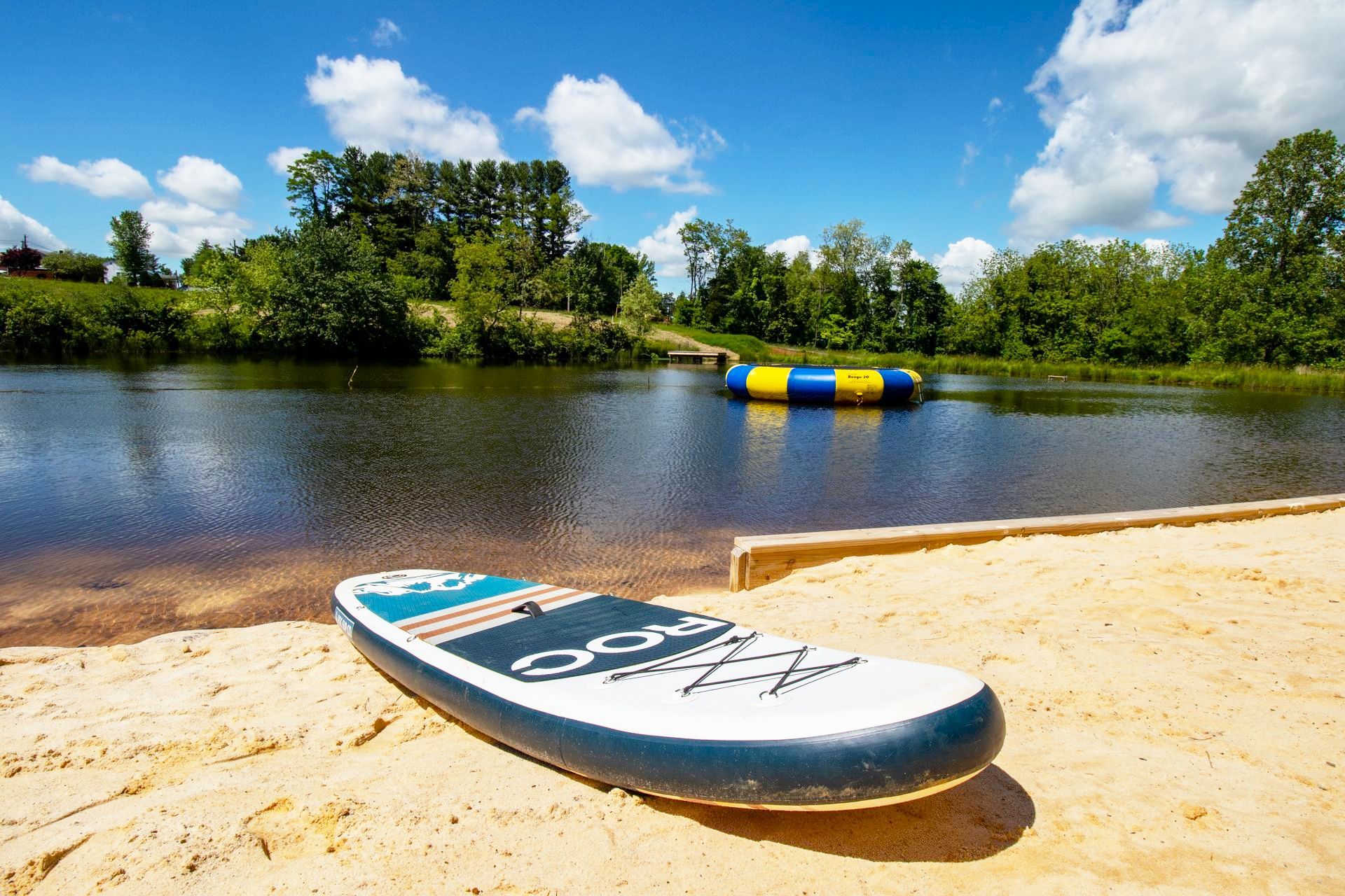 A surfboard is sitting on a sandy beach next to a lake.