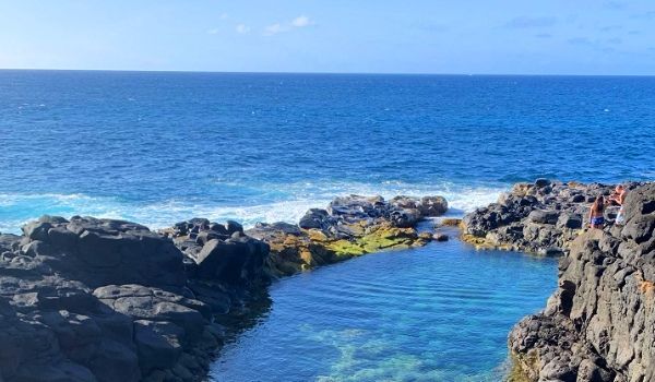 Rocky coastline with a clear, blue tide pool and ocean waves.