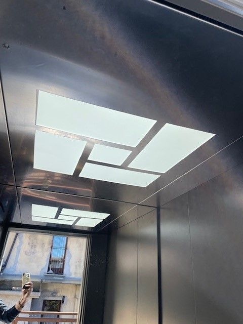 Interno di un ascensore con pareti a specchio e luci geometriche sul soffitto. Vista dalla finestra.