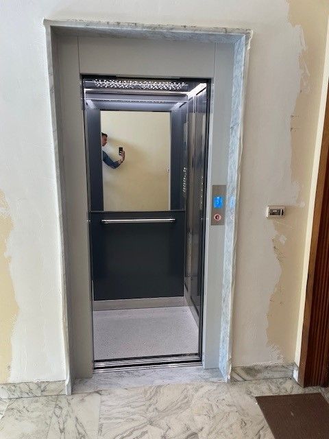 Porta dell'ascensore: un ascensore grigio all'interno di un edificio, con una persona riflessa nella porta dell'ascensore.