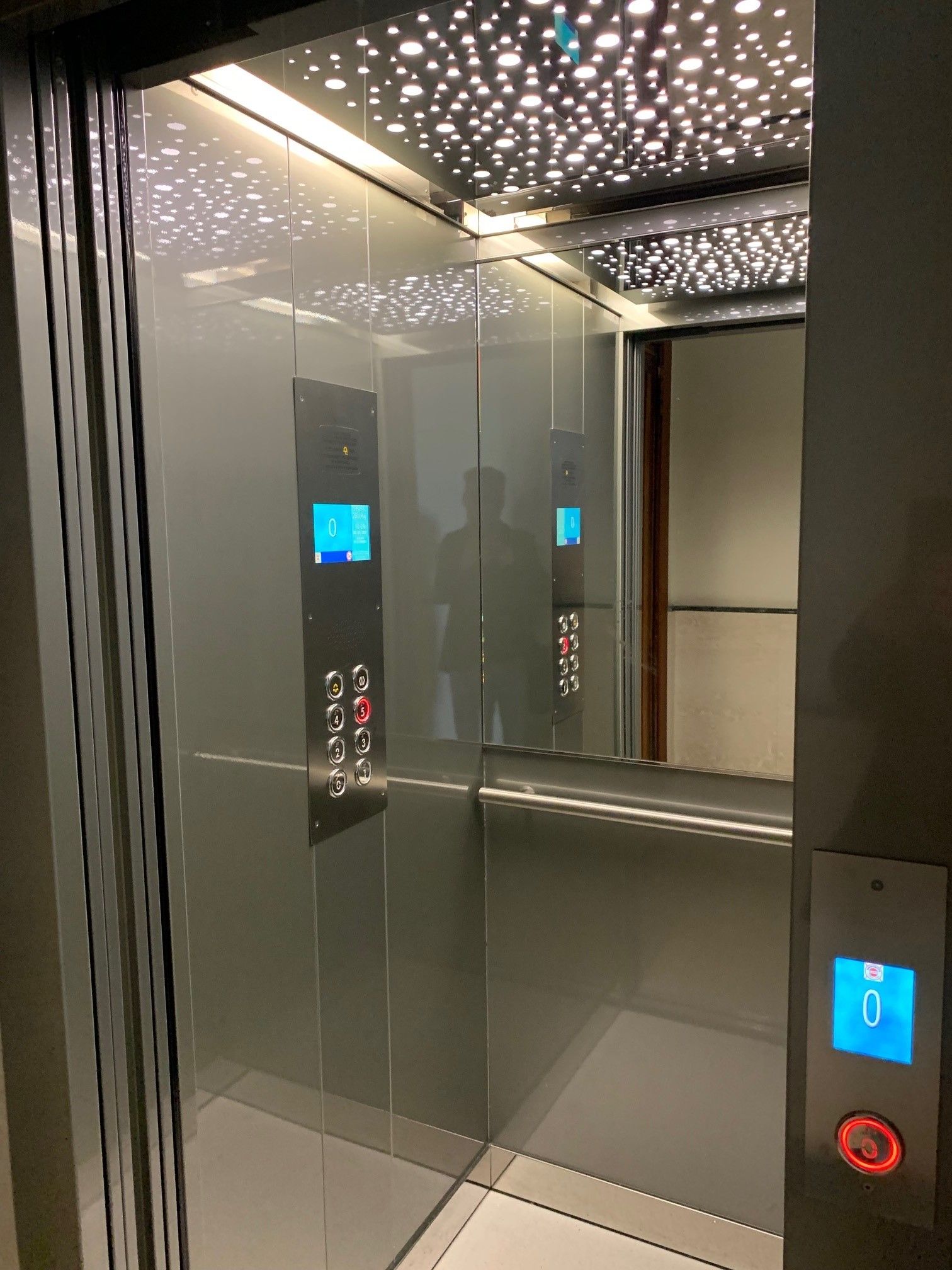 Interno dell'ascensore con soffitto stellato e indicatori di piano digitali. Pareti e pulsanti in metallo riflettente.