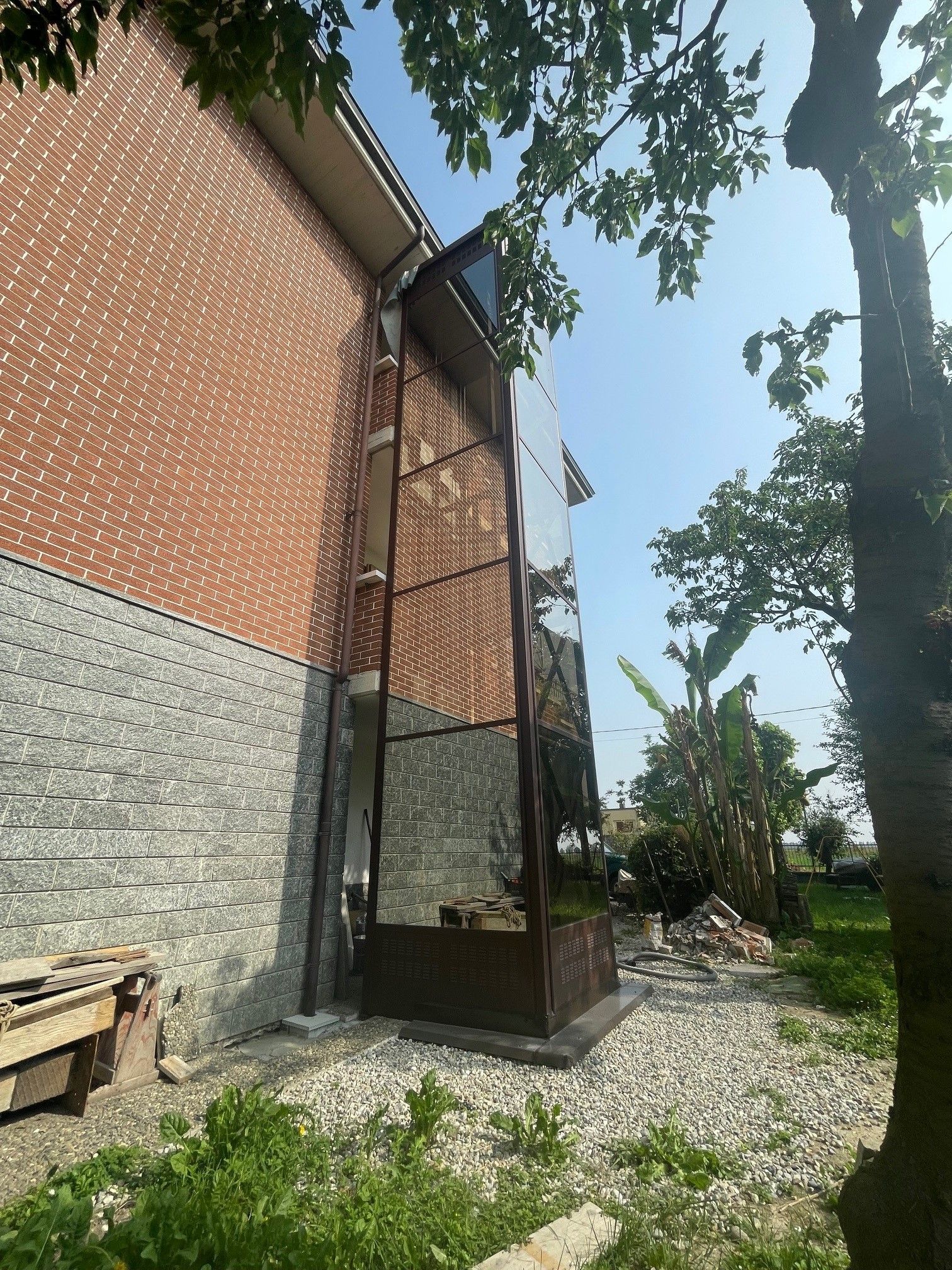 Esterno dell'edificio in mattoni e pietra, una struttura alta e stretta e un sentiero di ghiaia. Giornata di sole con alberi.