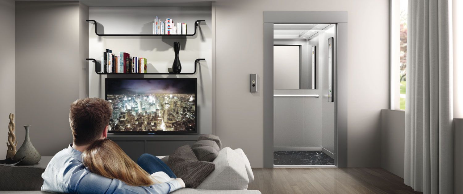Una coppia guarda la TV in un soggiorno con un ascensore visibile sulla destra.