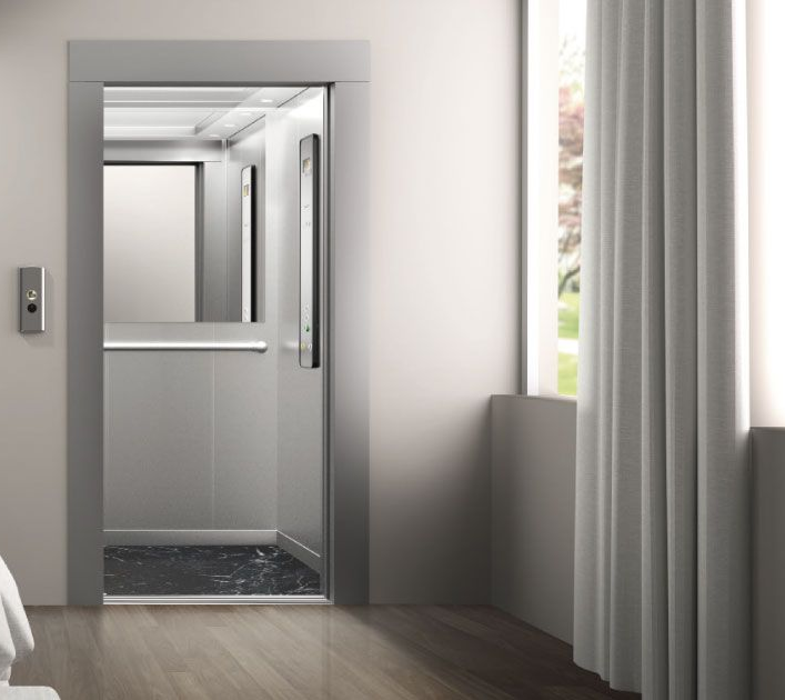 Porta dell'ascensore in una stanza luminosa con una pulsantiera sulla parete sinistra e tende sulla parete destra.