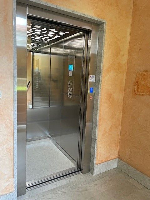 Un moderno ascensore con porte in acciaio inossidabile. All'interno dell'ascensore si possono vedere i pulsanti di controllo e un apparecchio di illuminazione.