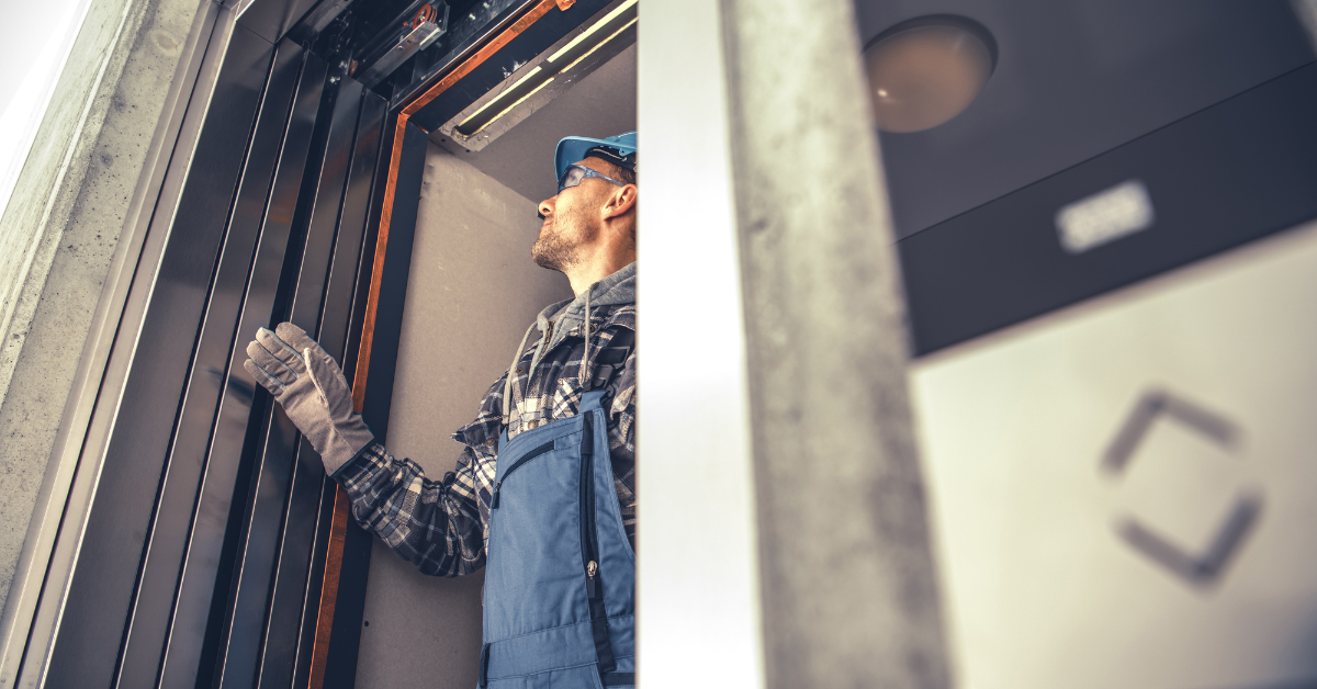 Tecnico dell'ascensore che ispeziona il vano ascensore; indossa un casco blu e una tuta.