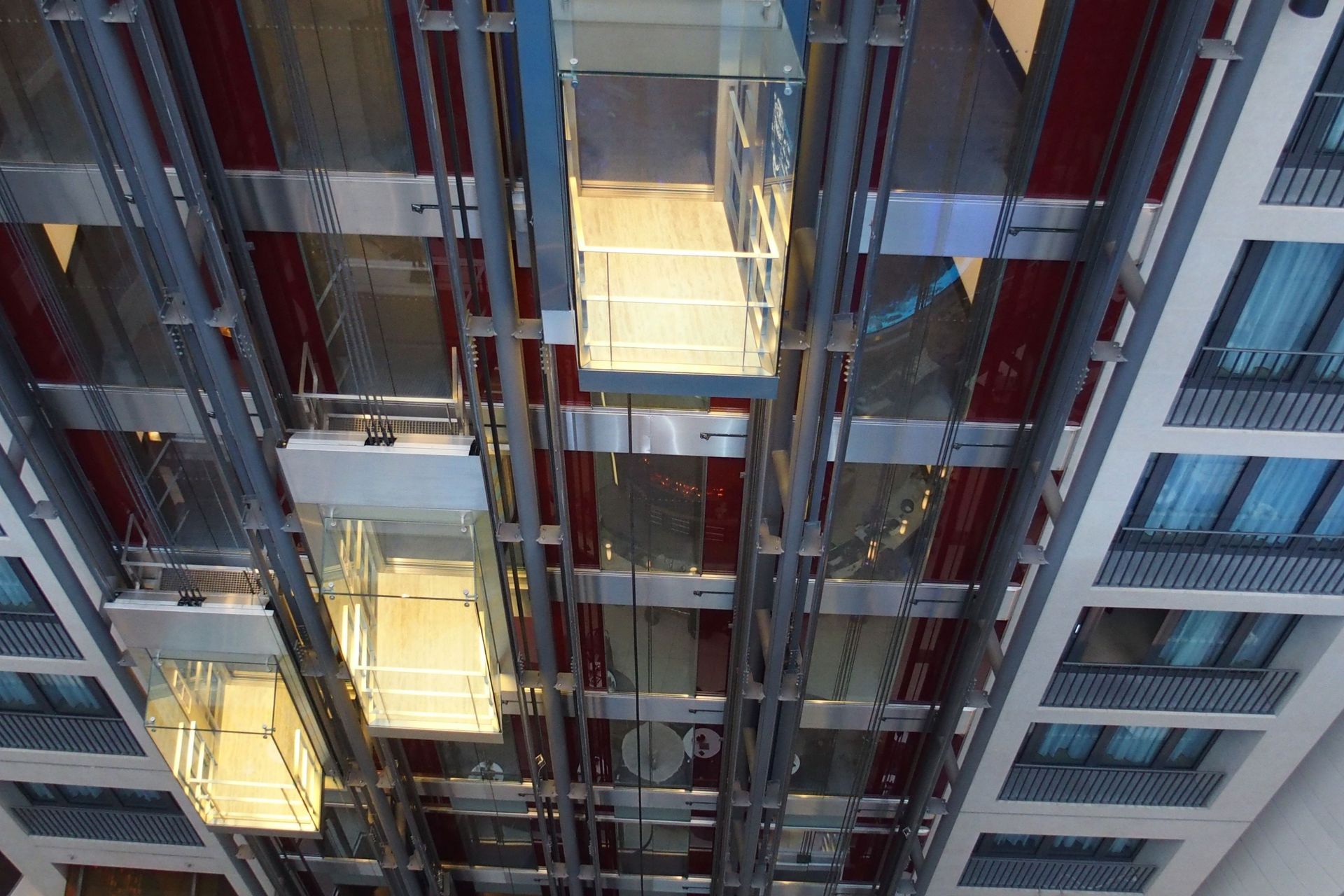 Ascensori in vetro che salgono e scendono all'interno di un edificio. Struttura in acciaio e rosso, finestre visibili.