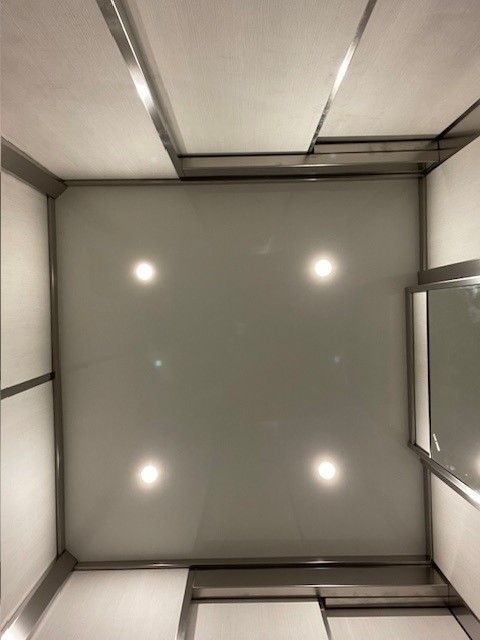 Soffitto dell'ascensore, vista verso l'alto. Pannelli bianchi, finiture cromate, quattro luci.