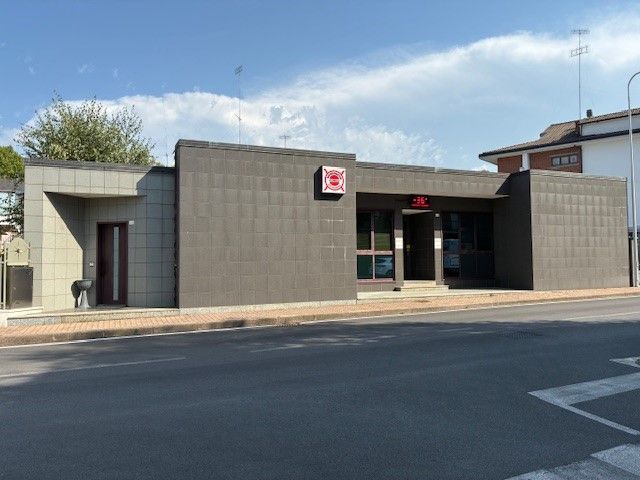 Vista esterna di un edificio a un piano con facciata in piastrelle grigie, dotato di porta e finestra; all'esterno c'è un cane.