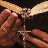 Mani di anziano con un libro aperto nelle mani del che pende un rosario