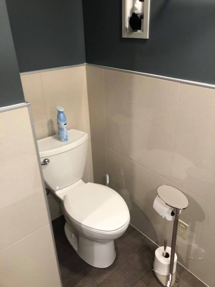 A bathroom with a toilet , toilet paper , and a spray bottle on the toilet.