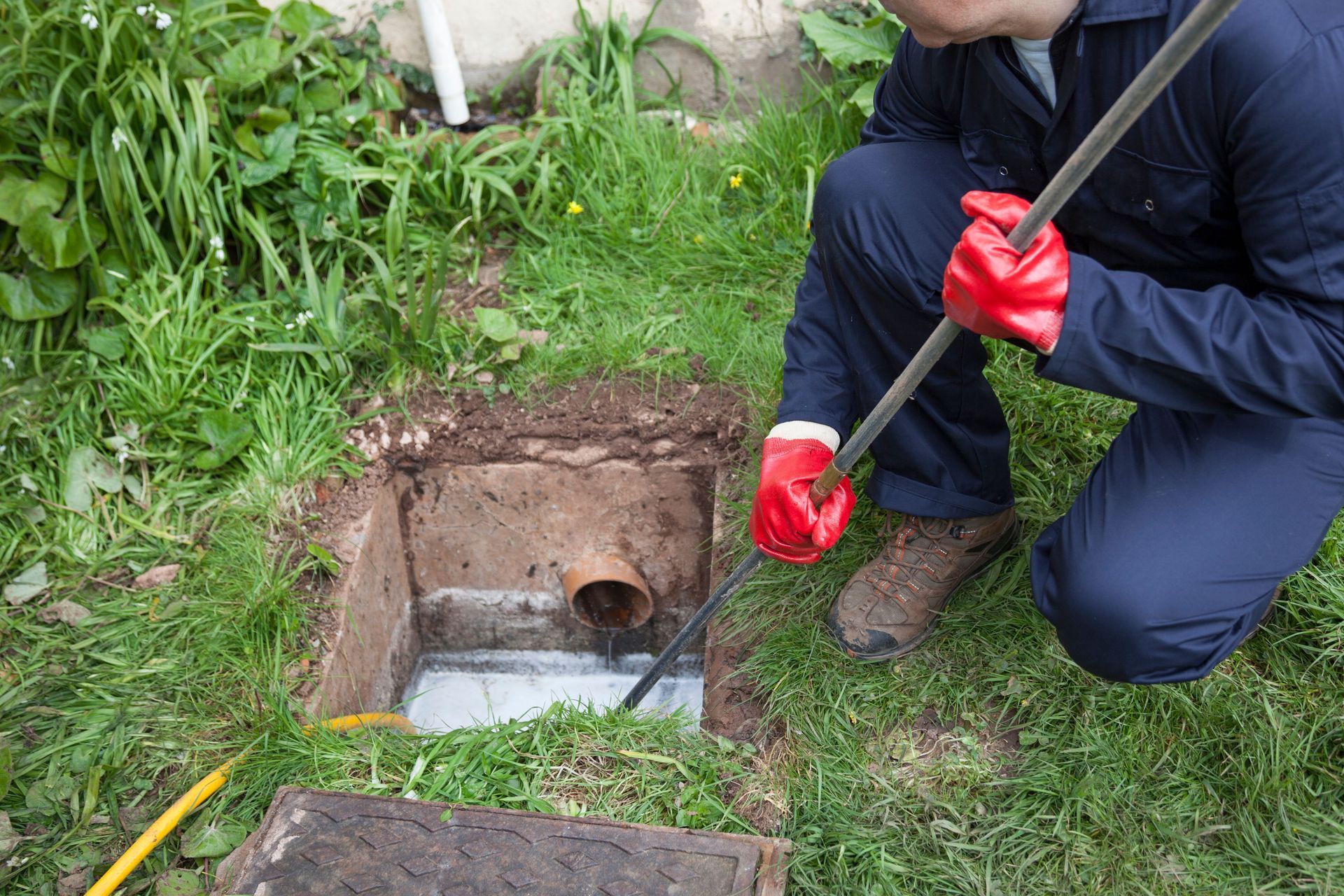 A man is kneeling down in the grass holding a hose.