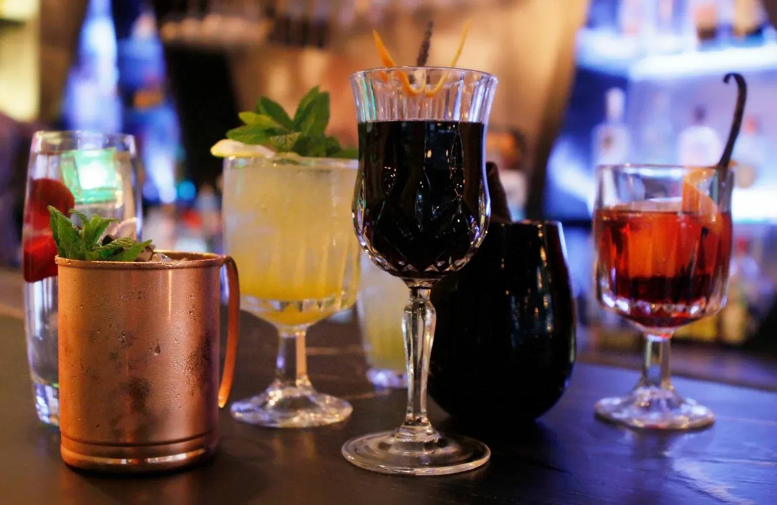 Cocktails on a bar: Copper mug, clear and colored glassware, dark and bright colors, garnishes.