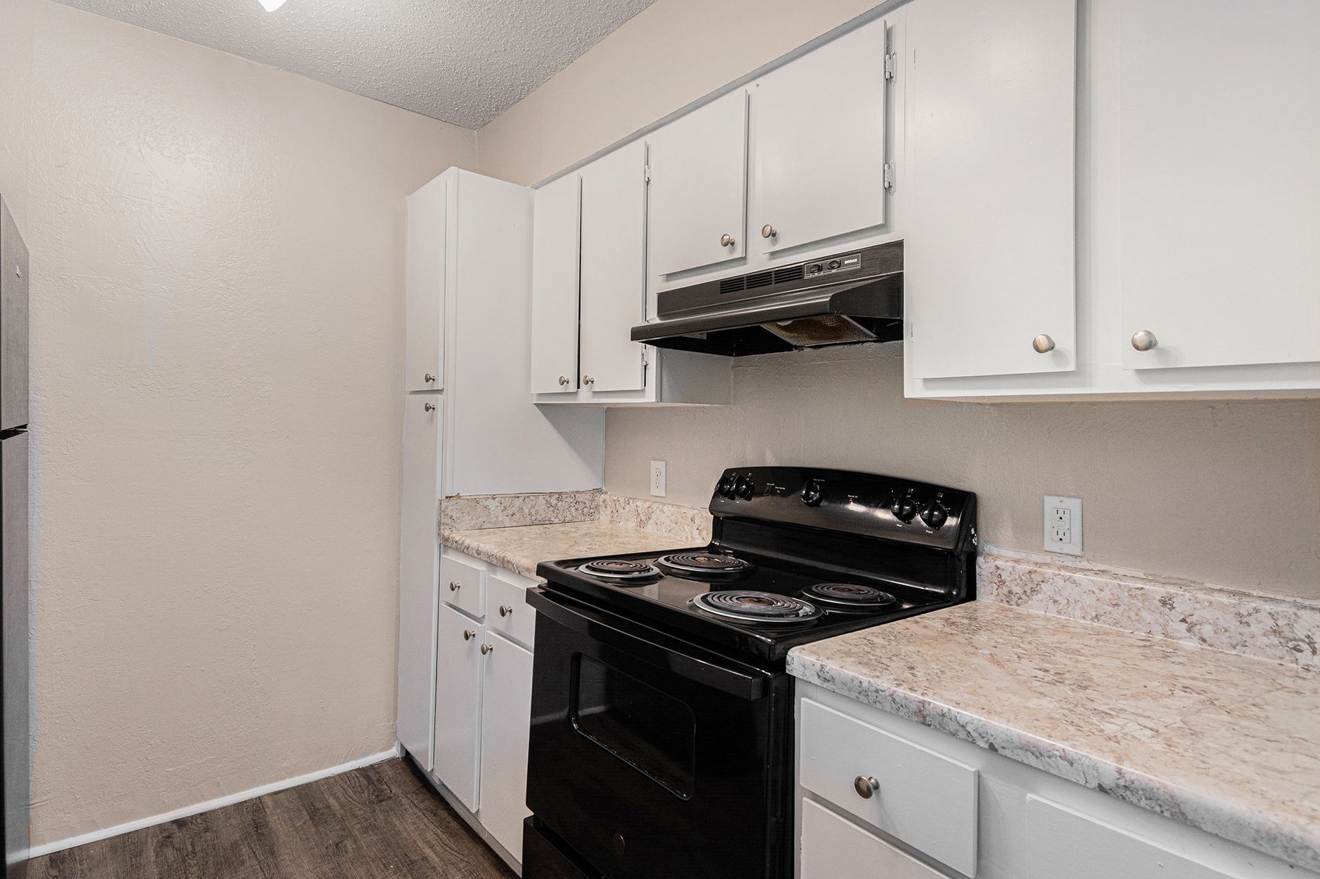 A kitchen featuring white cabinets, a black stove with a range hood, and light patterned countertops.