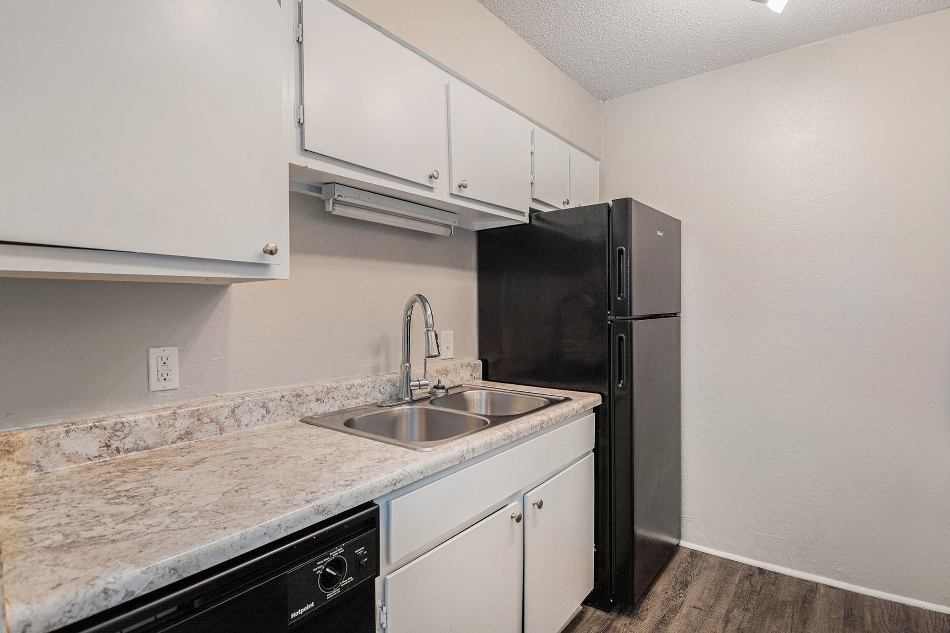 A kitchen featuring white cabinets, a black refrigerator, a stainless steel sink, and speckled granite countertops.