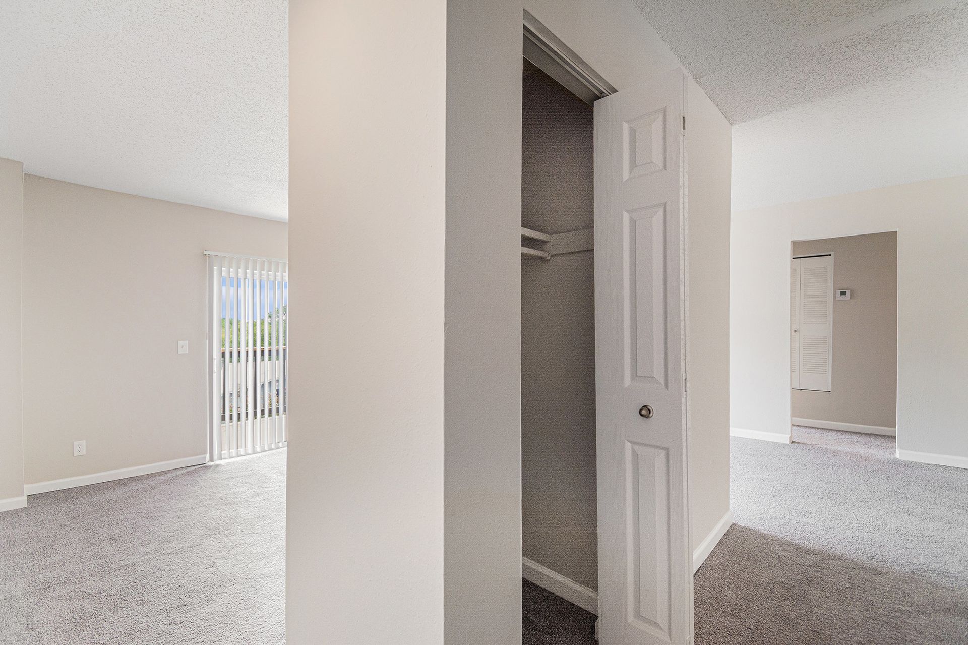 An interior view of a room with beige carpet, white walls, a closet with bifold doors, and a sliding glass balcony door.