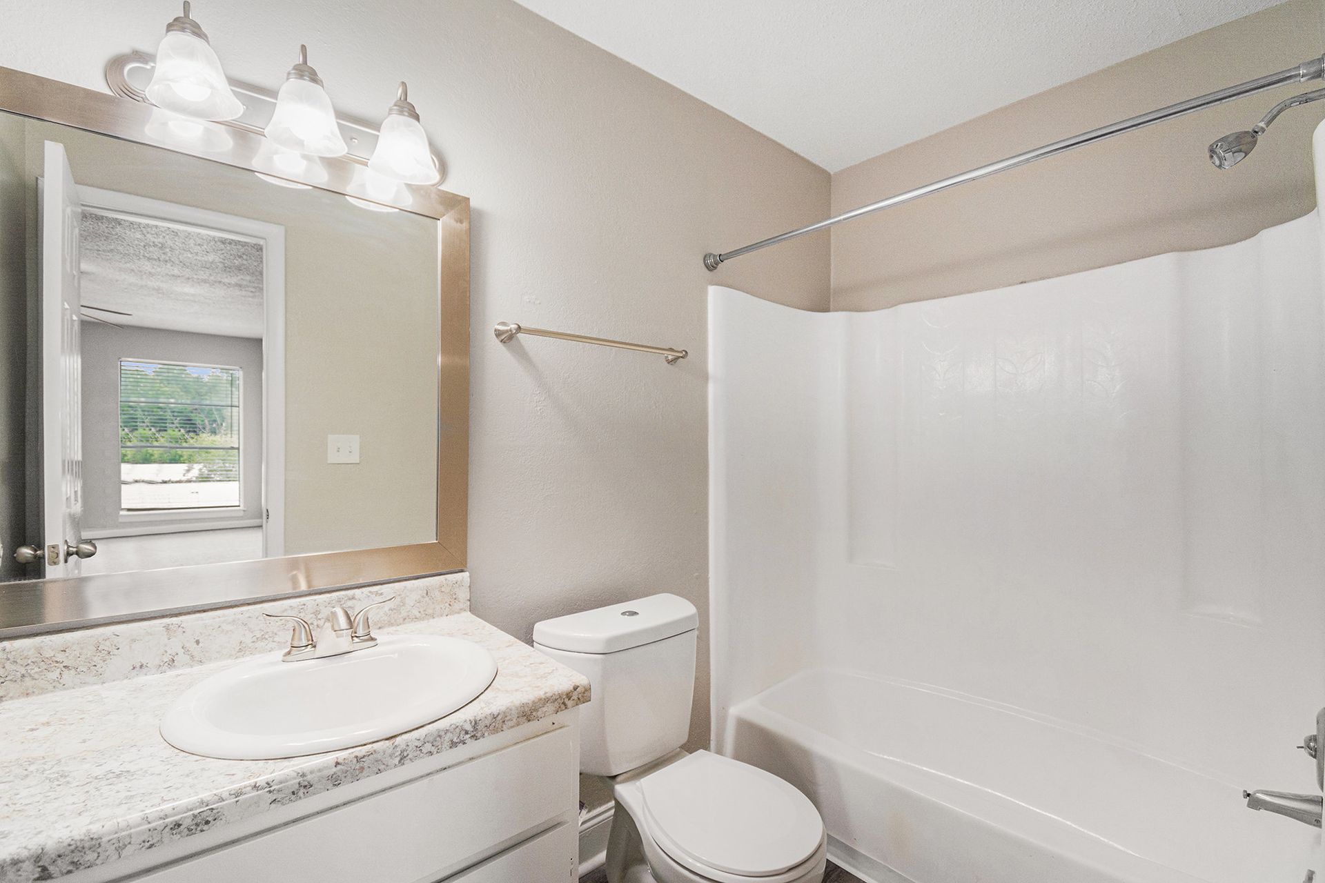 A bathroom featuring a light-colored vanity with a sink, a toilet, and a white shower-tub unit against beige walls.