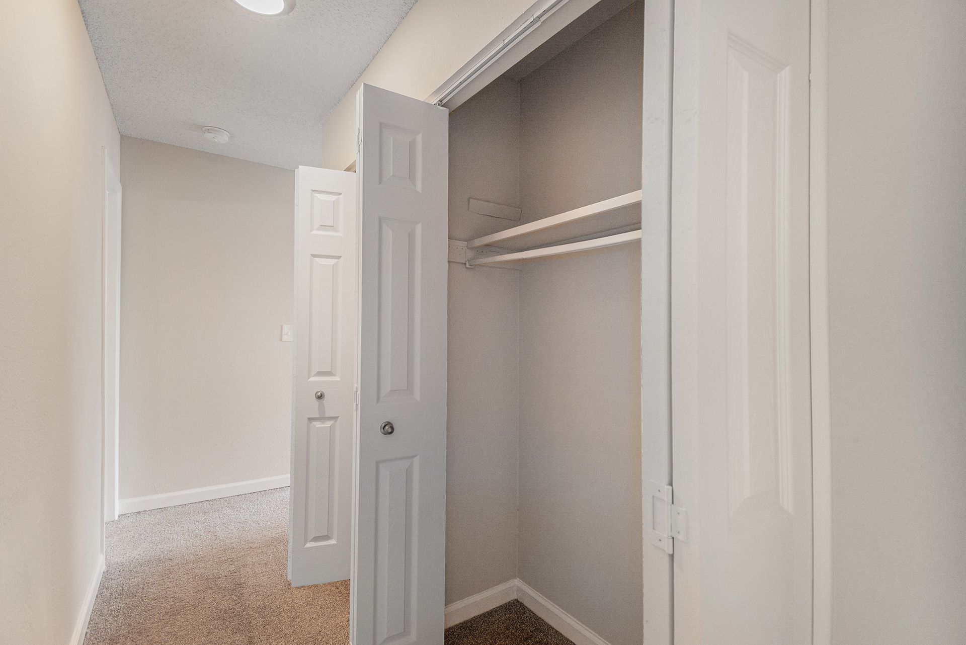 A beige hallway with a closet featuring white, open-hinged doors and a built-in shelving unit.