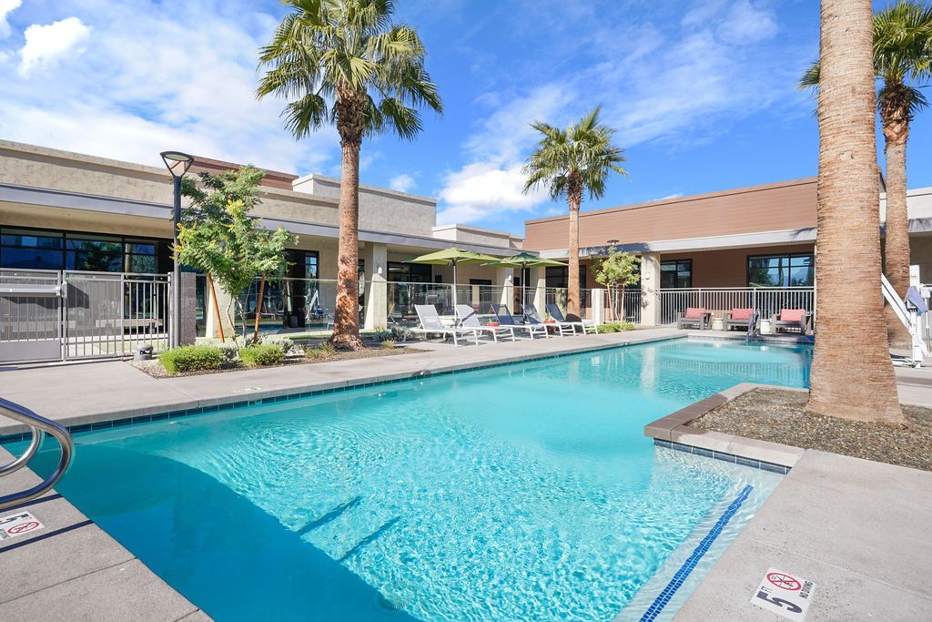 Outdoor pool area at a modern apartment community with sun loungers and palm trees.