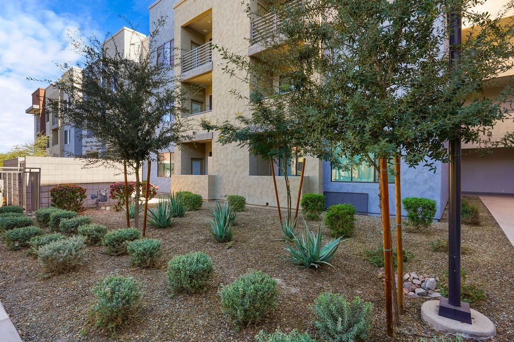 Exterior view of a modern apartment building with desert landscaping and trees.