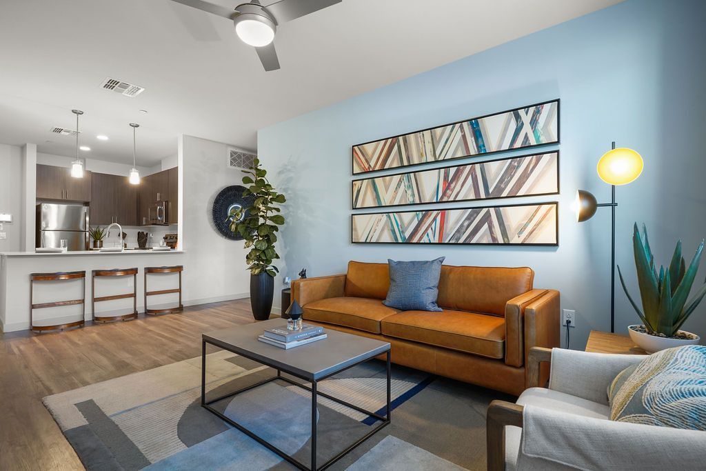 Open-concept living room with an orange sofa, blue accent wall, and a kitchen visible in the background.