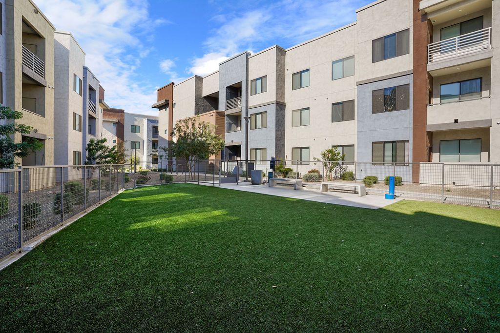 Courtyard with artificial turf, benches, and a fence-lined walkway between modern apartment buildings.