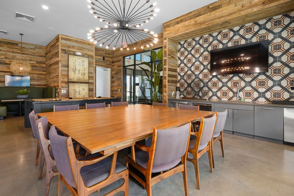 Modern community lounge with a large wooden table, TV, and geometric wall accents.