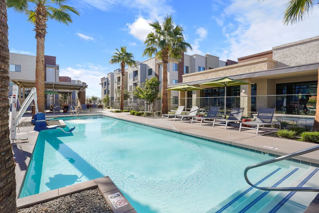 Outdoor pool at a modern apartment community with lounge chairs and palm trees.