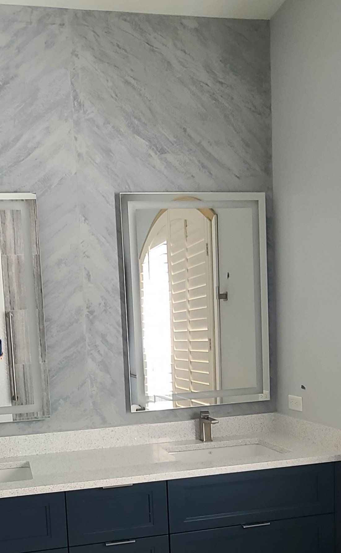 Bathroom with marble tile wall, mirror, vanity with blue cabinets and white countertop.