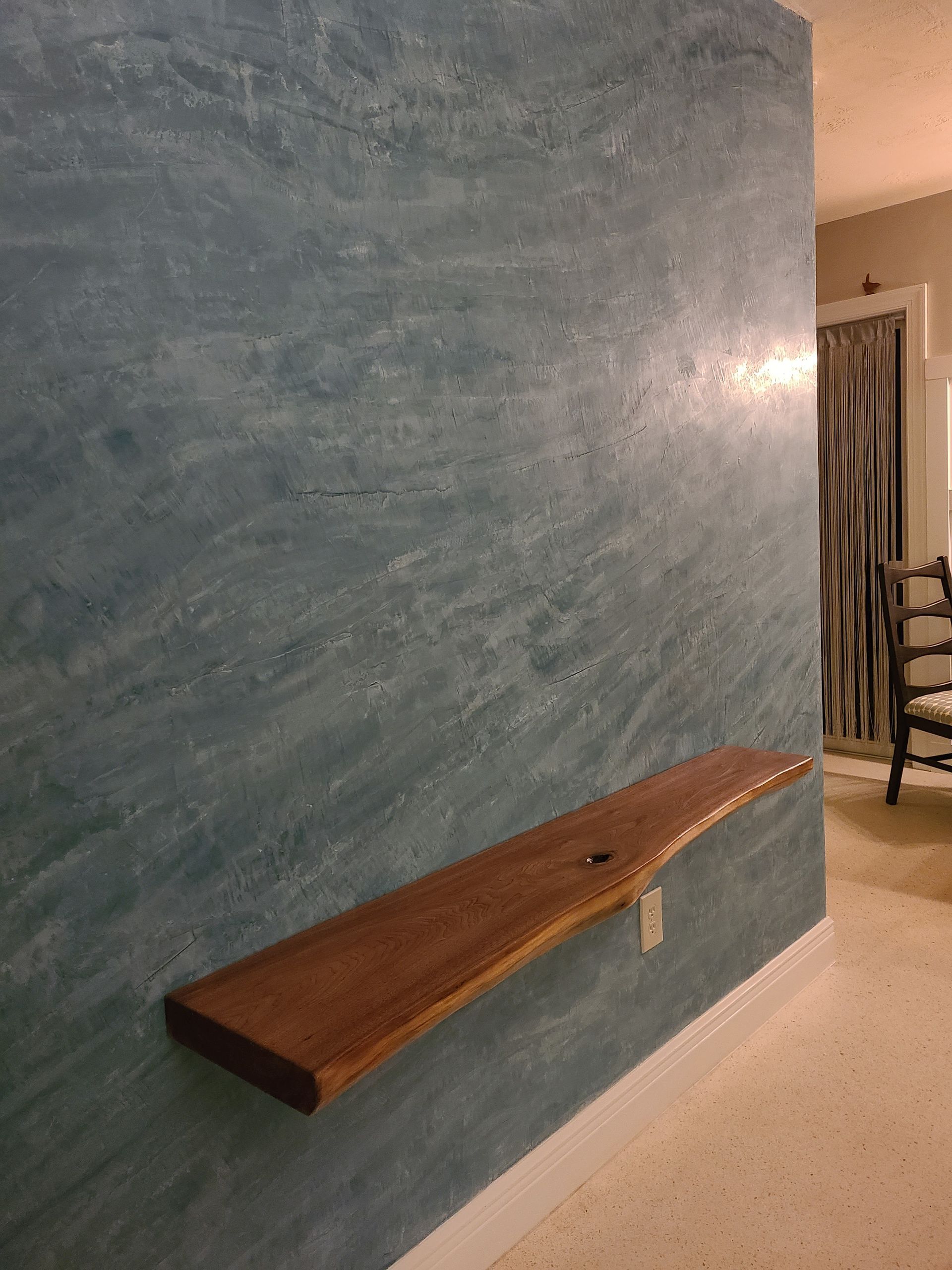 A blue textured wall with a brown floating wooden shelf, indoors.