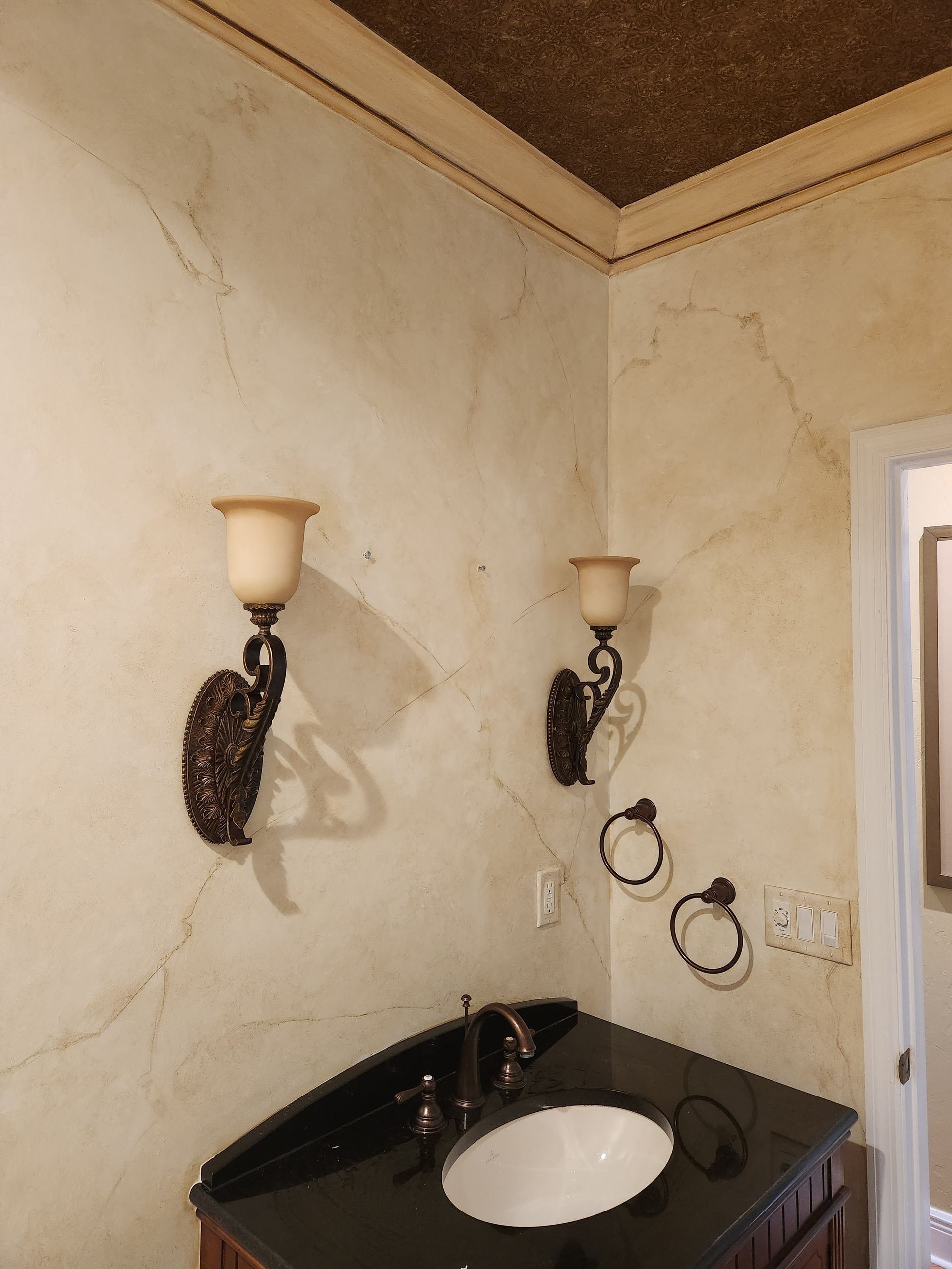 Bathroom with ornate sconces, dark vanity, and faux-finished walls; a textured ceiling.