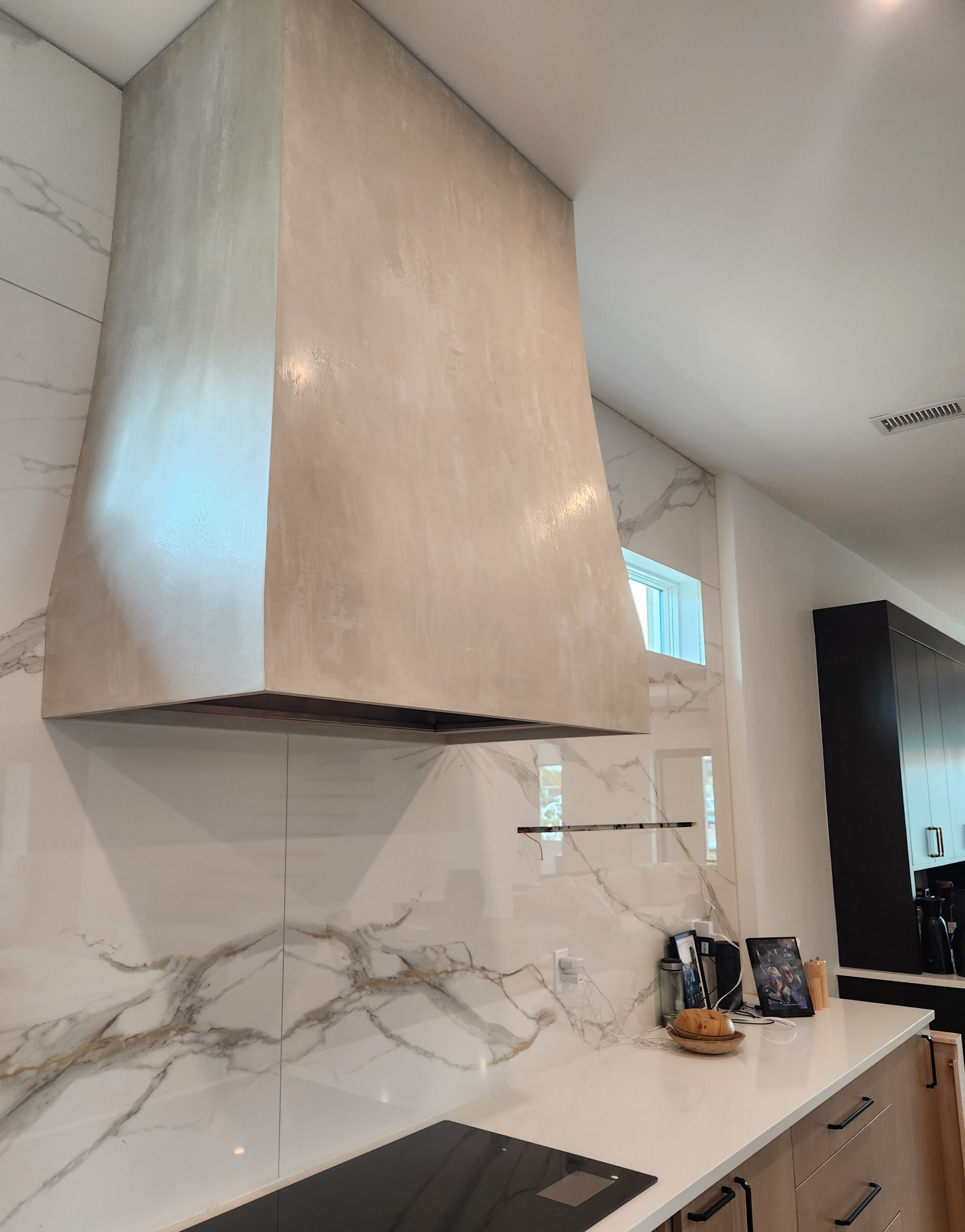 Cream-colored range hood above a white countertop with marble veining, in a modern kitchen.