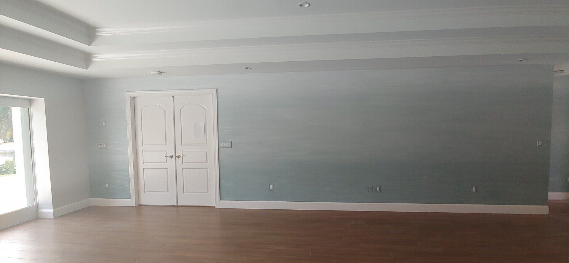Empty, pale blue room with white doors, trim and ceiling, and wooden floor.