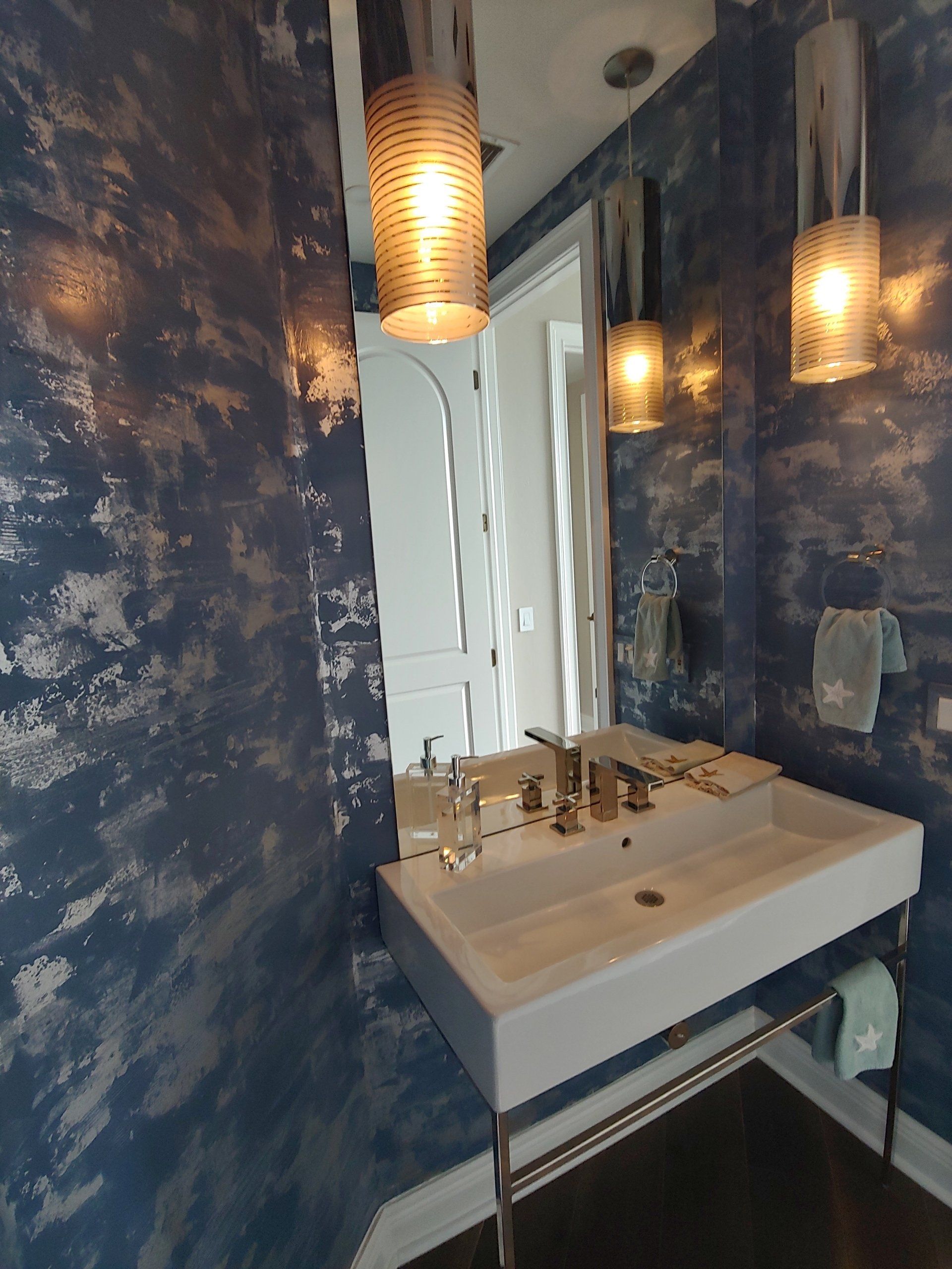 Blue and silver textured bathroom with a modern white sink, mirror, and hanging lights.