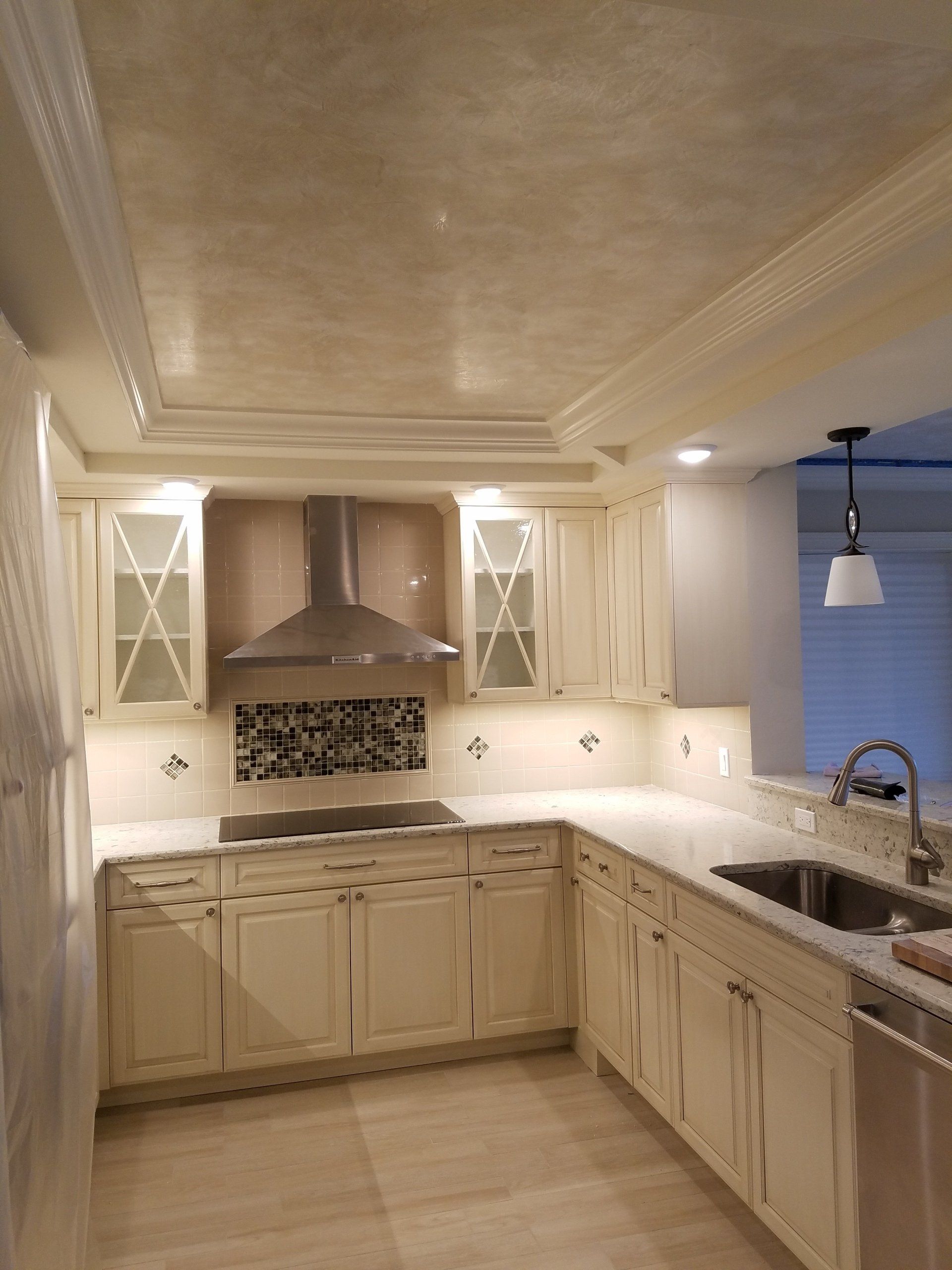Cream-colored kitchen with light countertops, cabinets, and a stainless steel range hood.