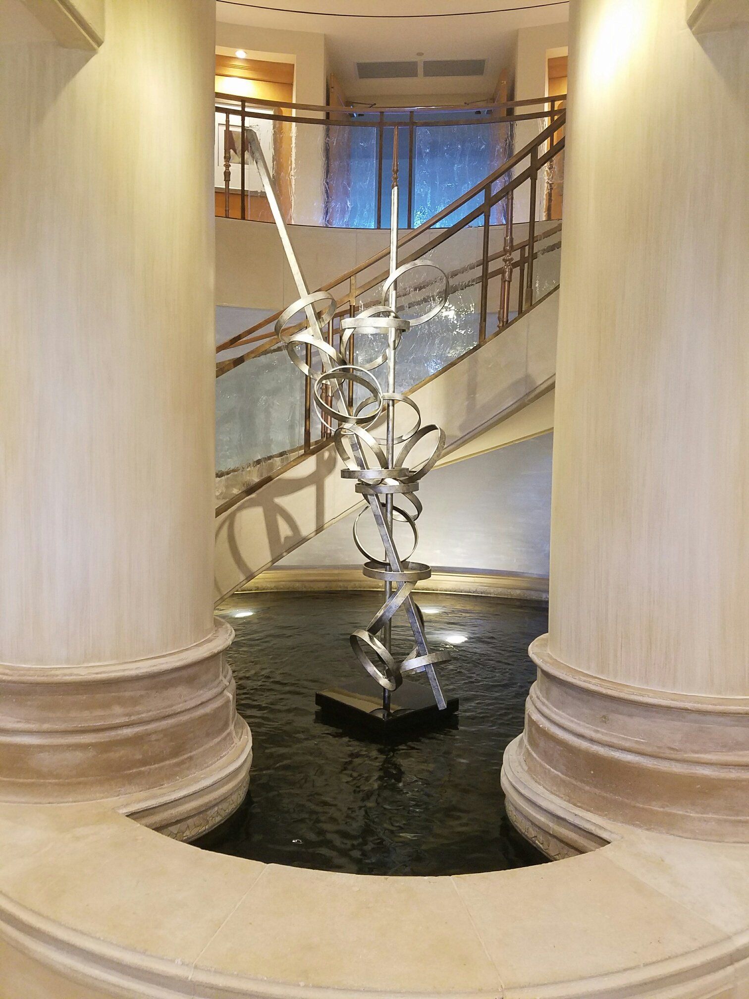 Sculpture in a fountain within a lobby, flanked by pillars, with stairs in the background.