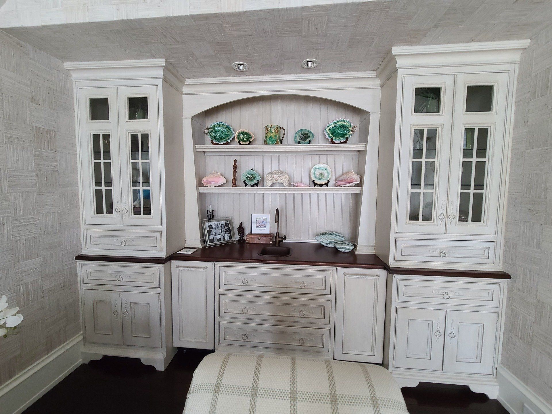 White built-in desk with cabinets, shelves displaying plates, and two side cabinets with glass doors.