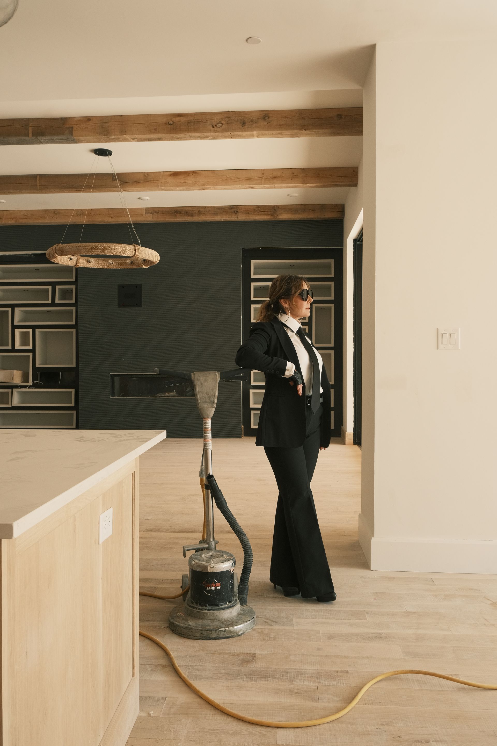 Stephanie Kratz in a suit is standing next to a floor sander in a newly built kitchen/living room.