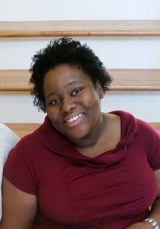 A woman in a red shirt is smiling in front of stairs