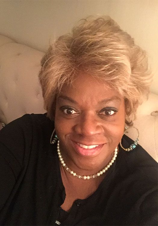 A woman wearing a wig and a pearl necklace is smiling for the camera.