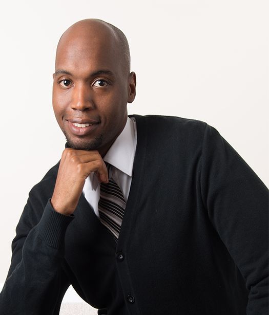 A man wearing a black sweater and tie with his hand on his chin